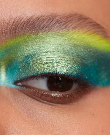 Close-up shot of a woman's eye with vibrant blue, green, and yellow eyeshadow, capturing the detail of the makeup and brow.
