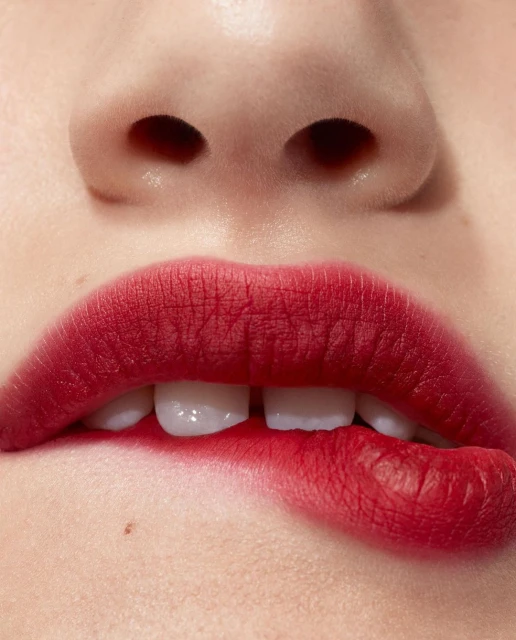 Extreme close-up of an adult female's face, emphasizing red lips with lipstick, white teeth, and pale skin, captured in bright light.