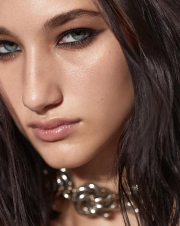 Close-up studio portrait of a young adult female with smokey eye makeup, dark hair, and a chunky silver chain necklace.