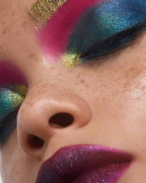 Close-up of a model wearing glittery gold, pink, and blue eyeshadow along with dark, sparkling lipstick in a beauty and makeup concept.