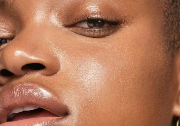 Extreme close-up portrait of a woman with glowing skin, subtle shimmering eyeshadow, and glossy lips photographed by Sarah Silver.