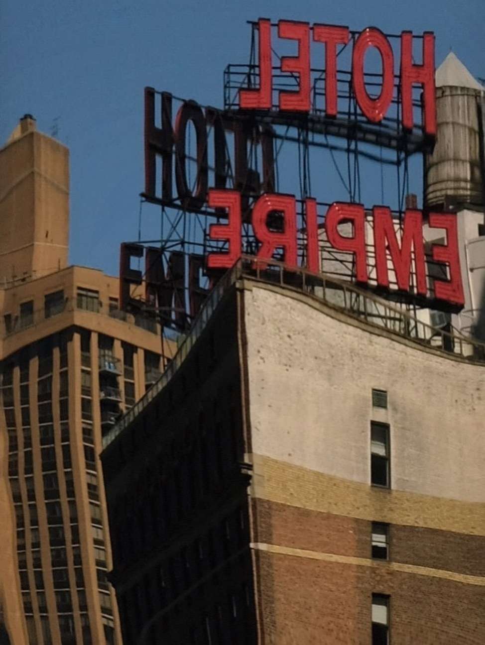 Urban landscape featuring the Empire Hotel sign atop a tall brick building against a blue sky in a city setting with other buildings.