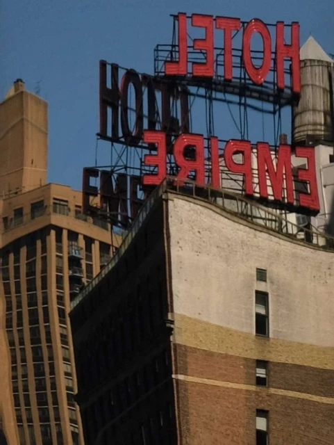 Urban landscape featuring the Empire Hotel sign atop a tall brick building against a blue sky in a city setting with other buildings.