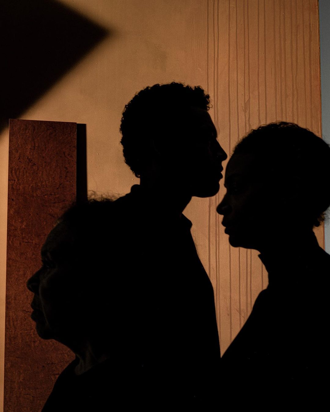 Silhouette of three people in profile against a textured wall with shadows. A family portrait captured in a low-key, artistic style.