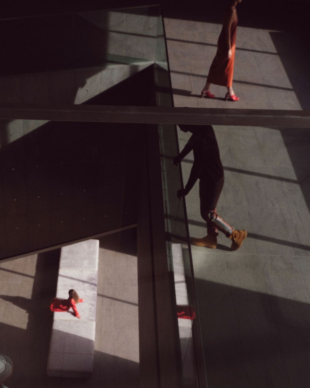 Low angle shot of two people walking on elevated walkways in a modern building, casting strong geometric shadows on the floor.