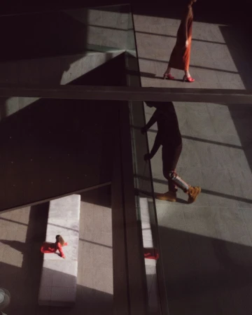 Low angle shot of two people walking on elevated walkways in a modern building, casting strong geometric shadows on the floor.