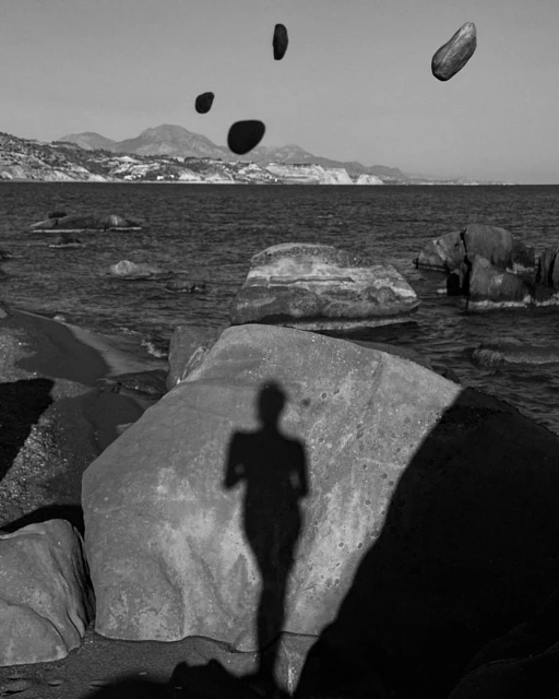 Black and white photo of a rocky beach landscape with an ocean view and the shadow of a person cast on a boulder.