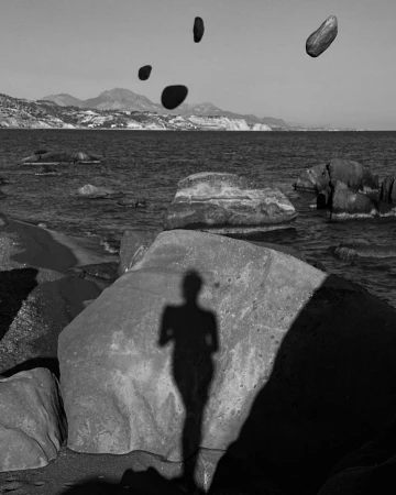 Black and white photo of a rocky beach landscape with an ocean view and the shadow of a person cast on a boulder.