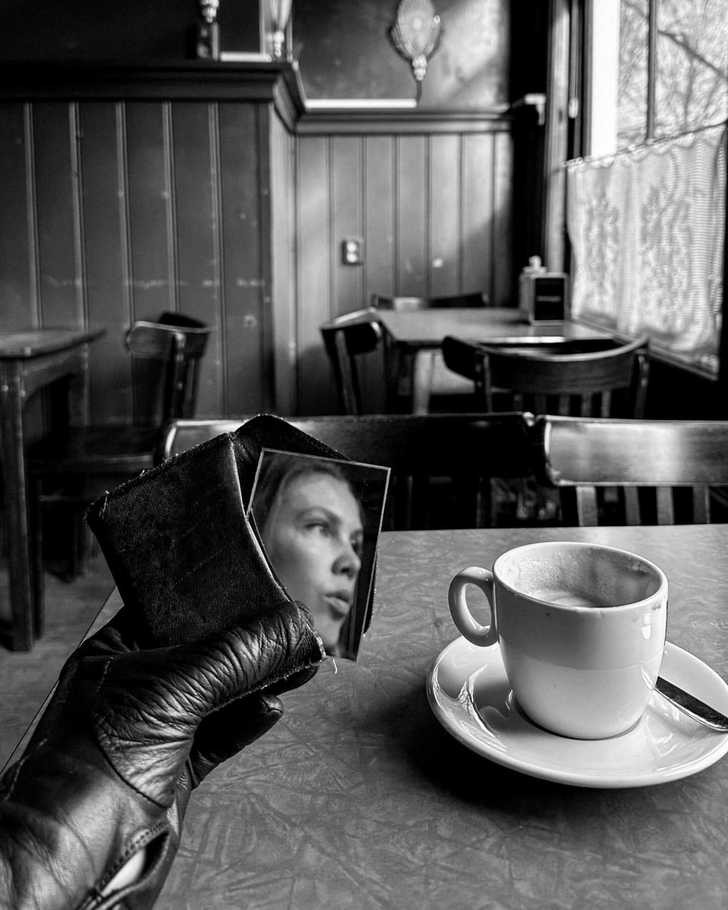 Monochromatic photo of a leather-gloved hand holding a wallet with a woman's image, juxtaposed with a cup of coffee in a cafe.