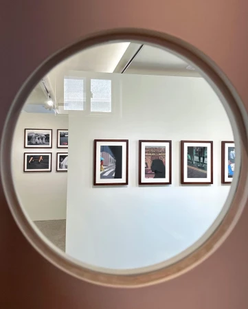 A view through a circular frame reveals an art gallery featuring framed photographs displayed on a white wall, illuminated by ceiling lights.