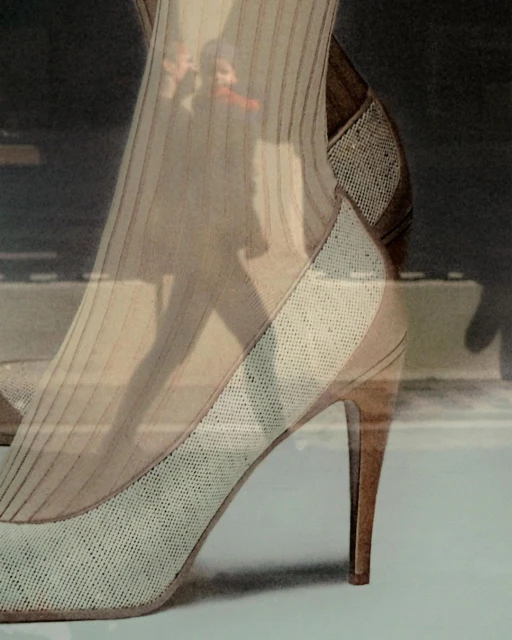 Elegant beige stiletto heel with a patterned texture, possibly a fashion product shot with an out-of-focus human silhouette background.