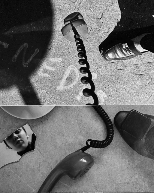High-angle, grayscale shot of a telephone receiver, shoes, and a person's reflection creating a surreal, dreamlike photographic composition.