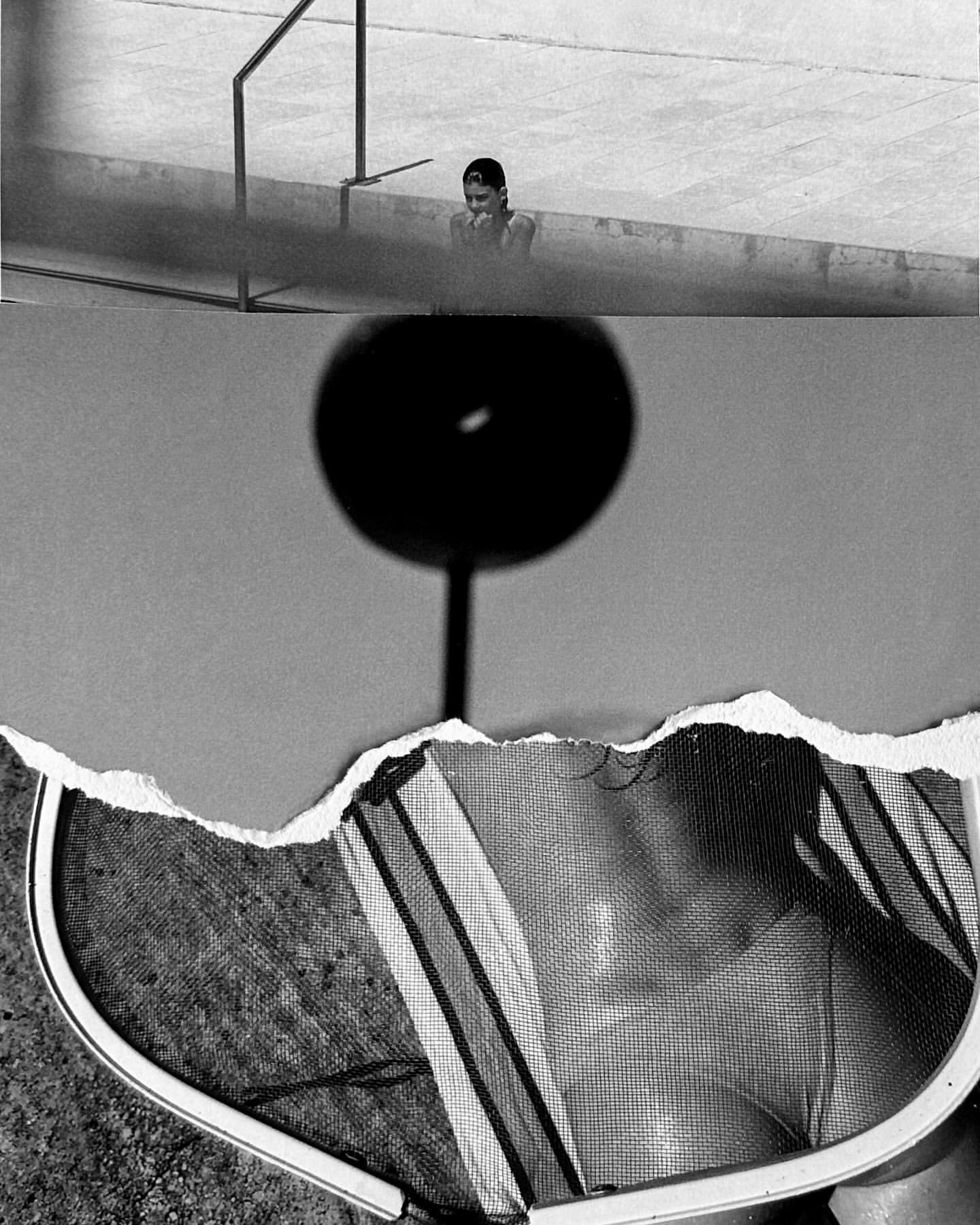 Black and white image of a woman partially submerged in a swimming pool, with a racquet in the foreground, shot with hard lighting.