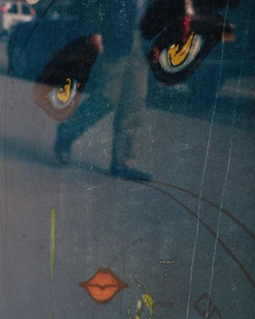 Abstract reflection of a person walking on a street, visible through a painted surface with eye and lip drawings.