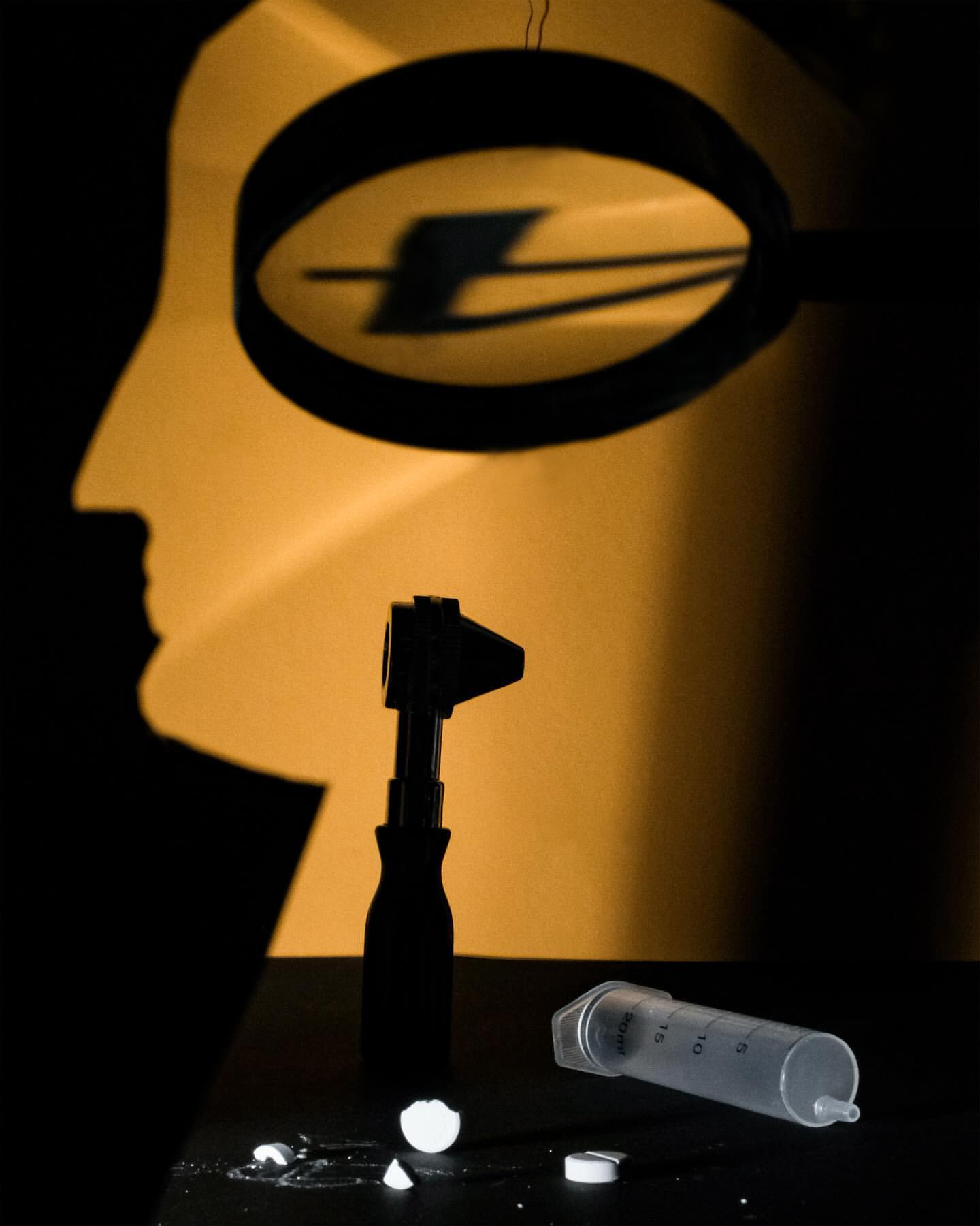 Medical still life featuring an otoscope, syringe, pills, and a head silhouette on a black surface against a gradient orange backdrop.