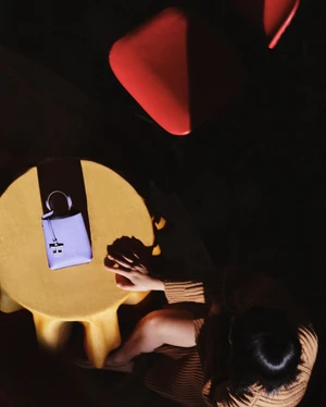Overhead view of a woman sitting at a yellow table beside a purple handbag, captured by Sarah Van Rij and David Van Der Leeuw.
