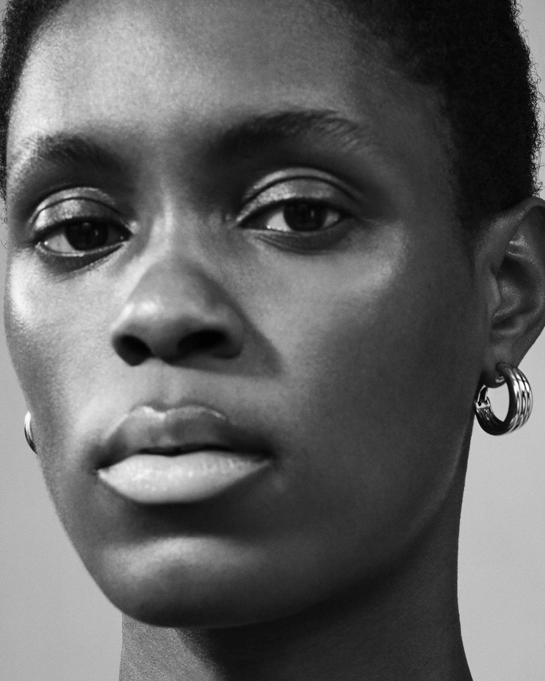 Close-up portrait of an adult African female with a neutral expression, wearing hoop earrings against a neutral background in black and white.