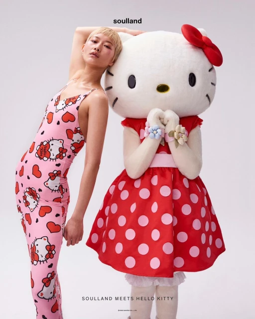 A woman with short blonde hair poses next to a costumed character of Hello Kitty wearing a red dress with white polka dots.