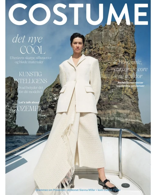 Fashion magazine cover featuring a woman in a cream-colored suit posing on a boat with a rocky coastline in the background.