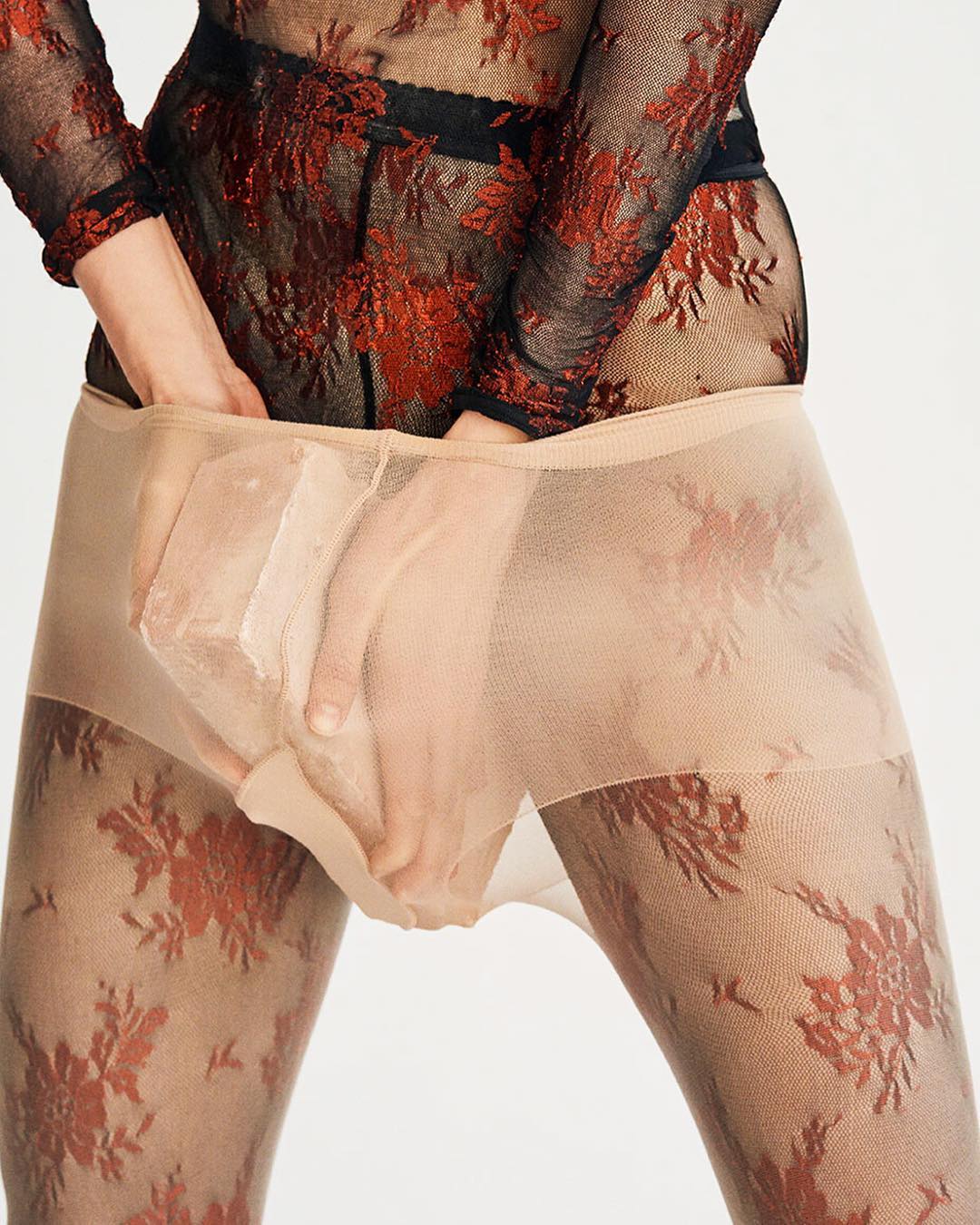 Close-up of a person wearing patterned hosiery and a sheer patterned top, with hands adjusting the waistband, set against a white background.