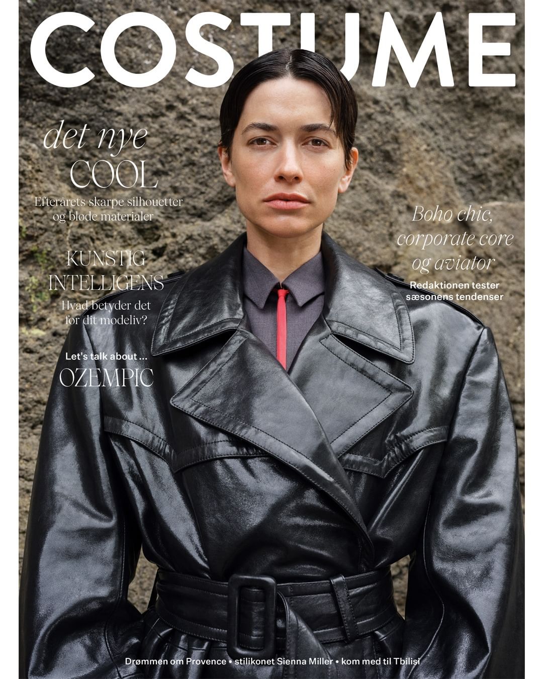 Magazine cover featuring a woman in a black leather trench coat against a textured stone background, with the 'COSTUME' logo.