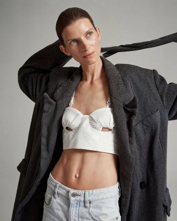 A stylish adult woman poses in a photo studio, wearing a gray blazer, white top, and jeans against a neutral backdrop.