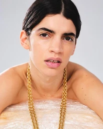 Portrait of a model wearing a heavy gold chain necklace against a light grey studio background.