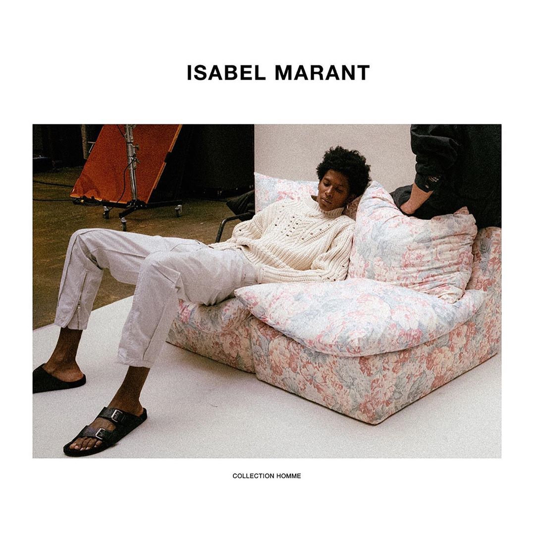 Man wearing a white sweater and light-colored pants lounging on a floral patterned sofa. Fashion editorial for Isabel Marant.