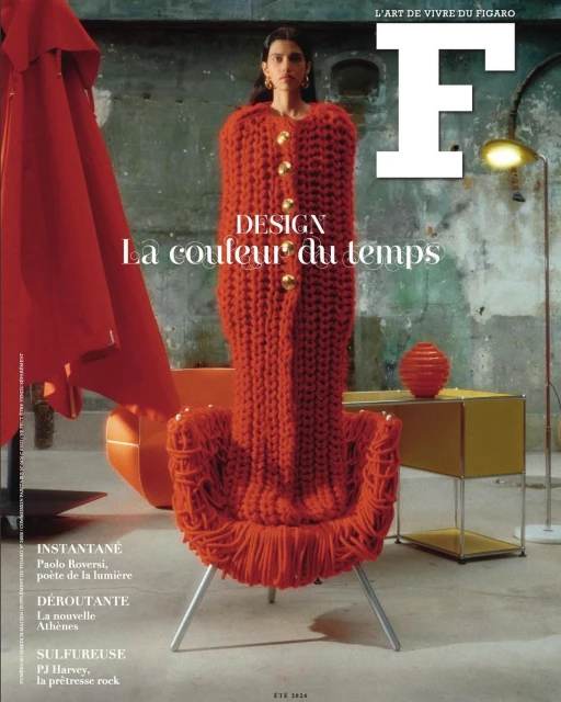 Magazine cover featuring a person in a textured, full-body orange knit garment, posing with an orange armchair and side table indoors.