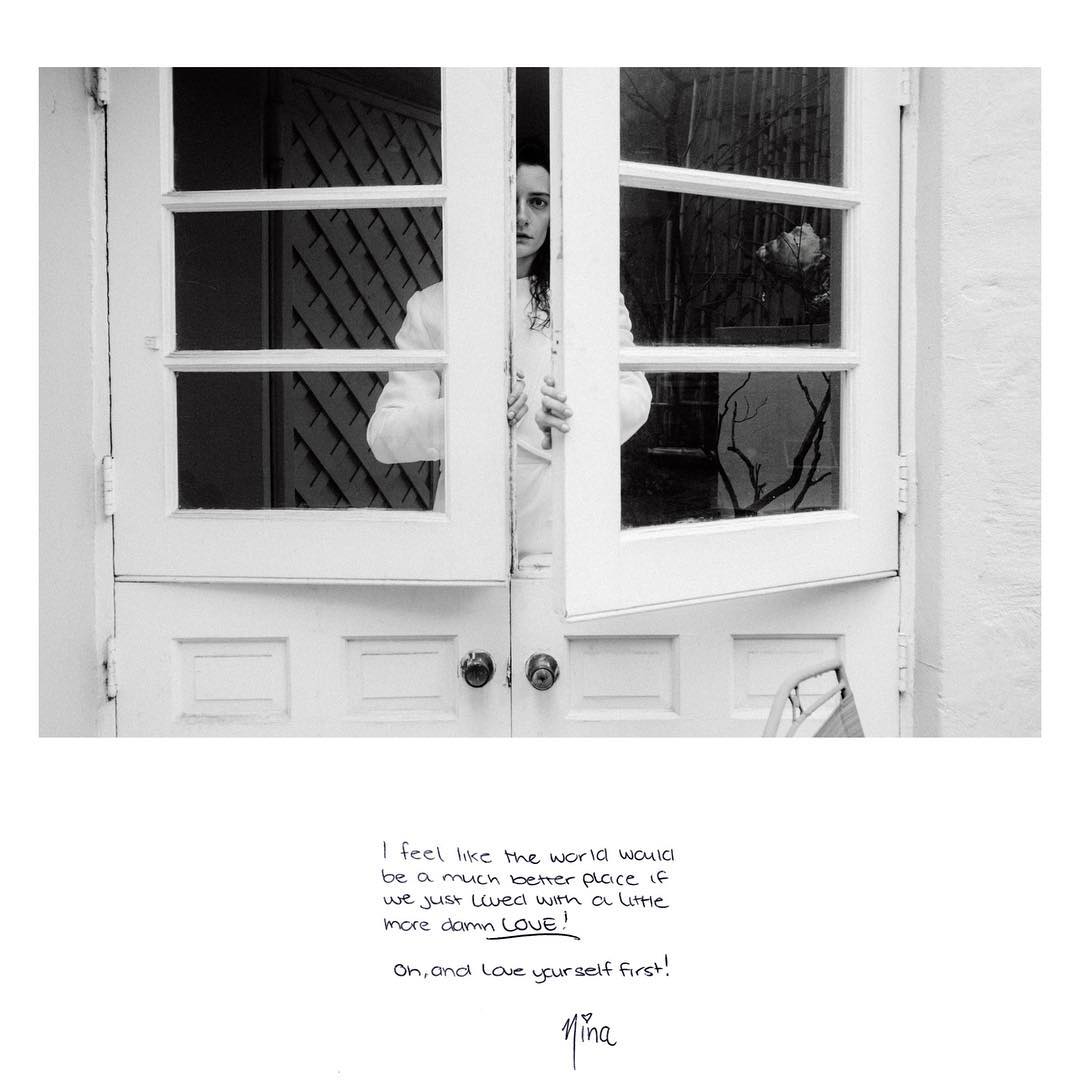 Monochrome portrait of a woman peering through an open white door. Natural light illuminates the scene and text appears below.