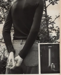 Close-up of a person wearing a dark long-sleeve top and houndstooth trousers with hands clasped behind back, against an outdoor background.