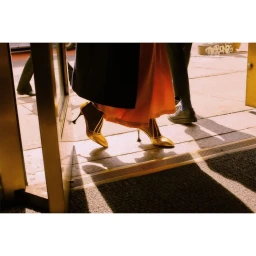 Close-up of a person walking through a doorway wearing gold high heels and a long skirt, captured in warm daylight by Sasha Lytvyn.