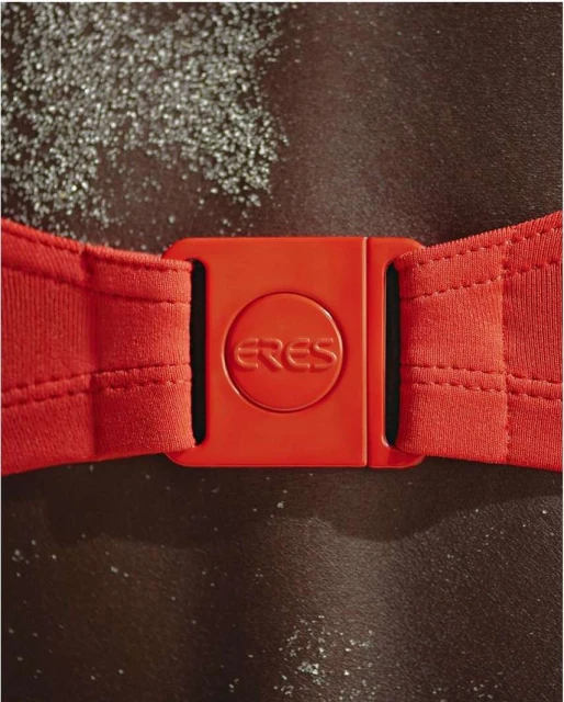 Close-up shot of a red Eres swimsuit clasp against dark skin and textured background, showcasing swimwear detail.