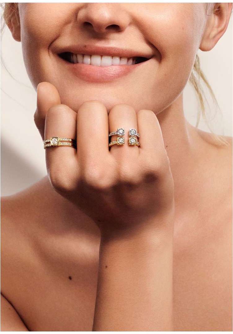 Close-up of a smiling adult female showcasing two gold and diamond rings, one worn on the ring finger and another on the middle finger.
