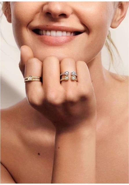 Close-up of a smiling adult female showcasing two gold and diamond rings, one worn on the ring finger and another on the middle finger.