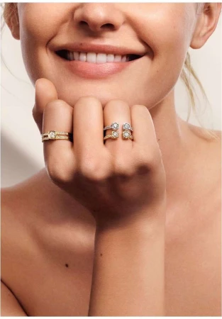 Close-up of a smiling adult female showcasing two gold and diamond rings, one worn on the ring finger and another on the middle finger.