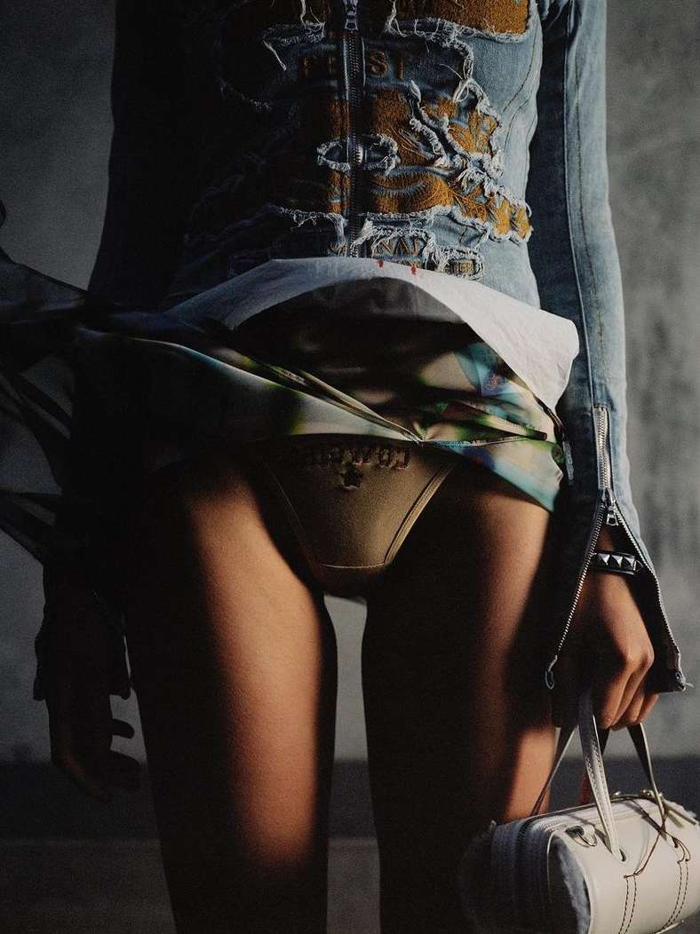 Fashion shot of a woman's lower torso, legs, and part of her hand holding a purse in an indoor studio setting.