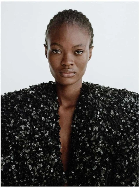 Close-up studio shot of an adult African-American woman wearing a black sequined jacket against a white background, showcasing fashion.