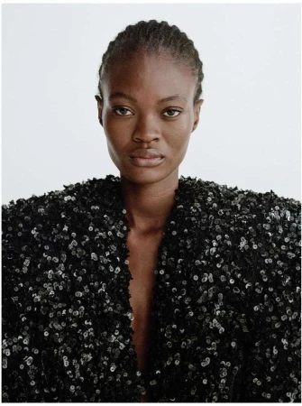 Close-up studio shot of an adult African-American woman wearing a black sequined jacket against a white background, showcasing fashion.