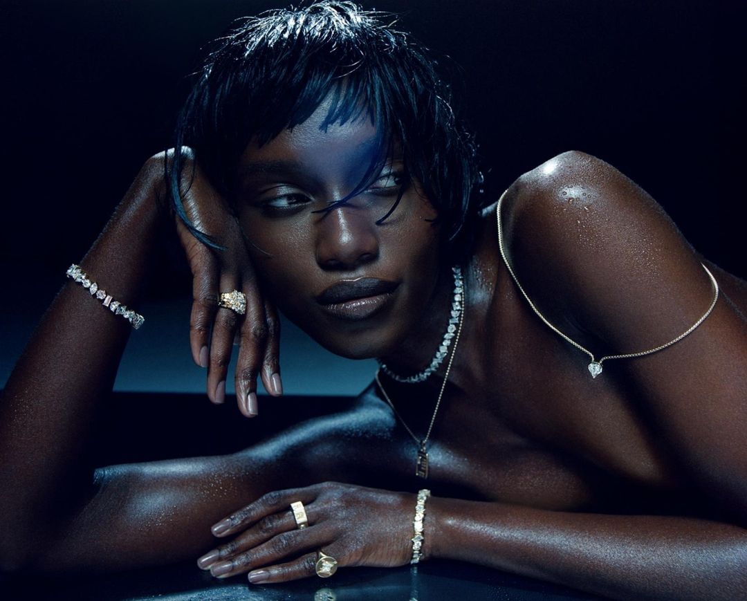 Elegant black woman with wet hair poses with diamond jewelry against a dark background. Jewelry includes rings, bracelet, and necklace.