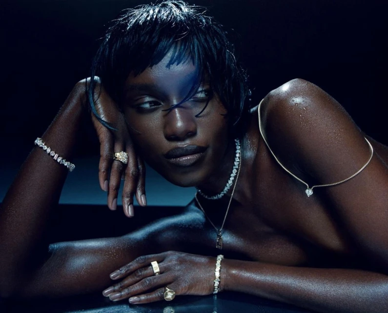 Elegant black woman with wet hair poses with diamond jewelry against a dark background. Jewelry includes rings, bracelet, and necklace.