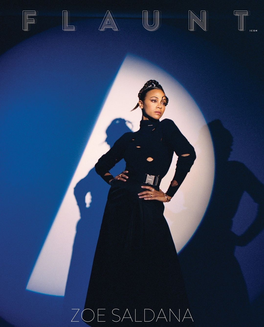 Zoe Saldana poses in a long black dress on a fashion magazine cover with blue lighting and the magazine title 'Flaunt' visible at the top.