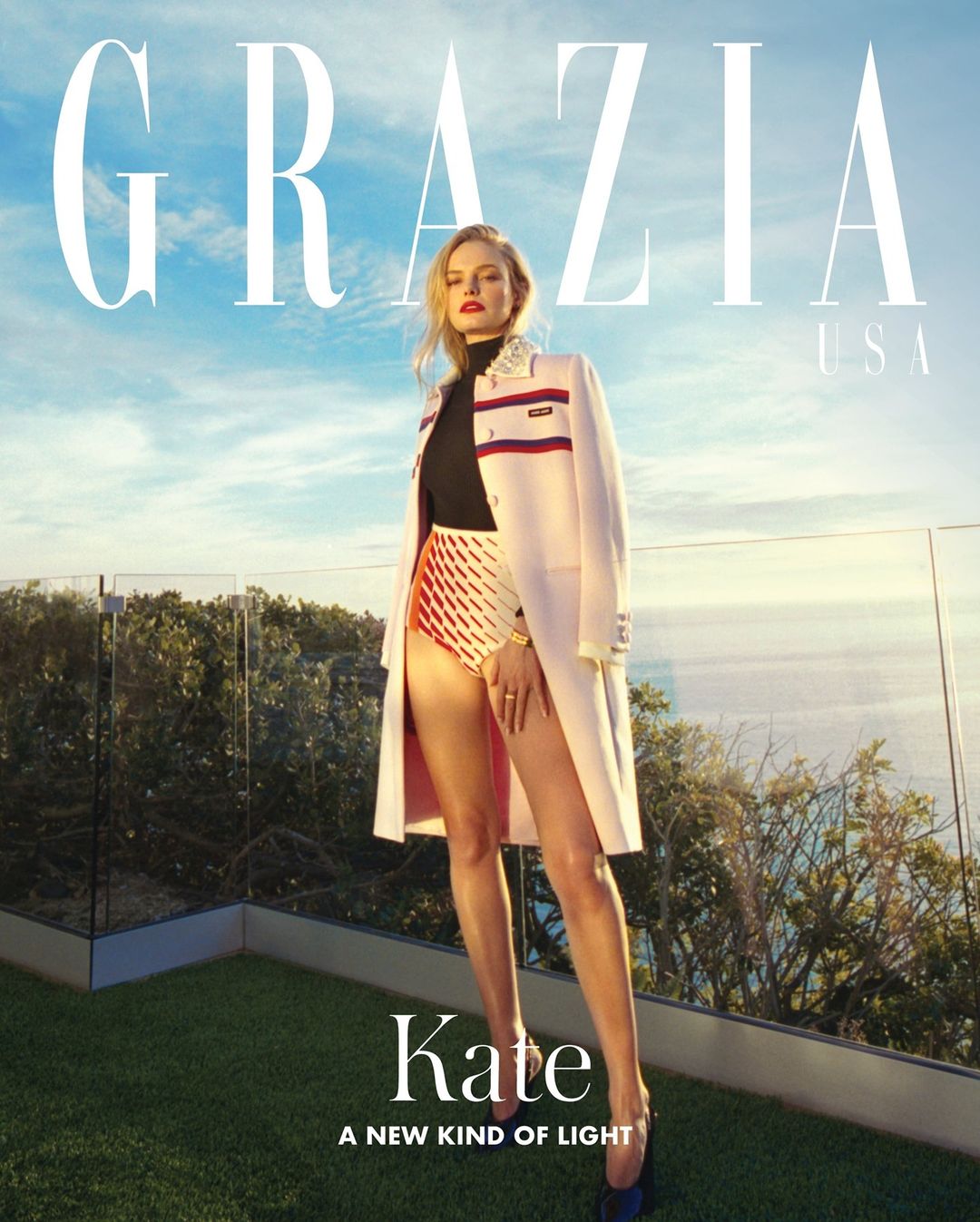 Blonde model poses outdoors on a rooftop in high-waisted shorts and a jacket for a magazine cover, with a blue sky backdrop.