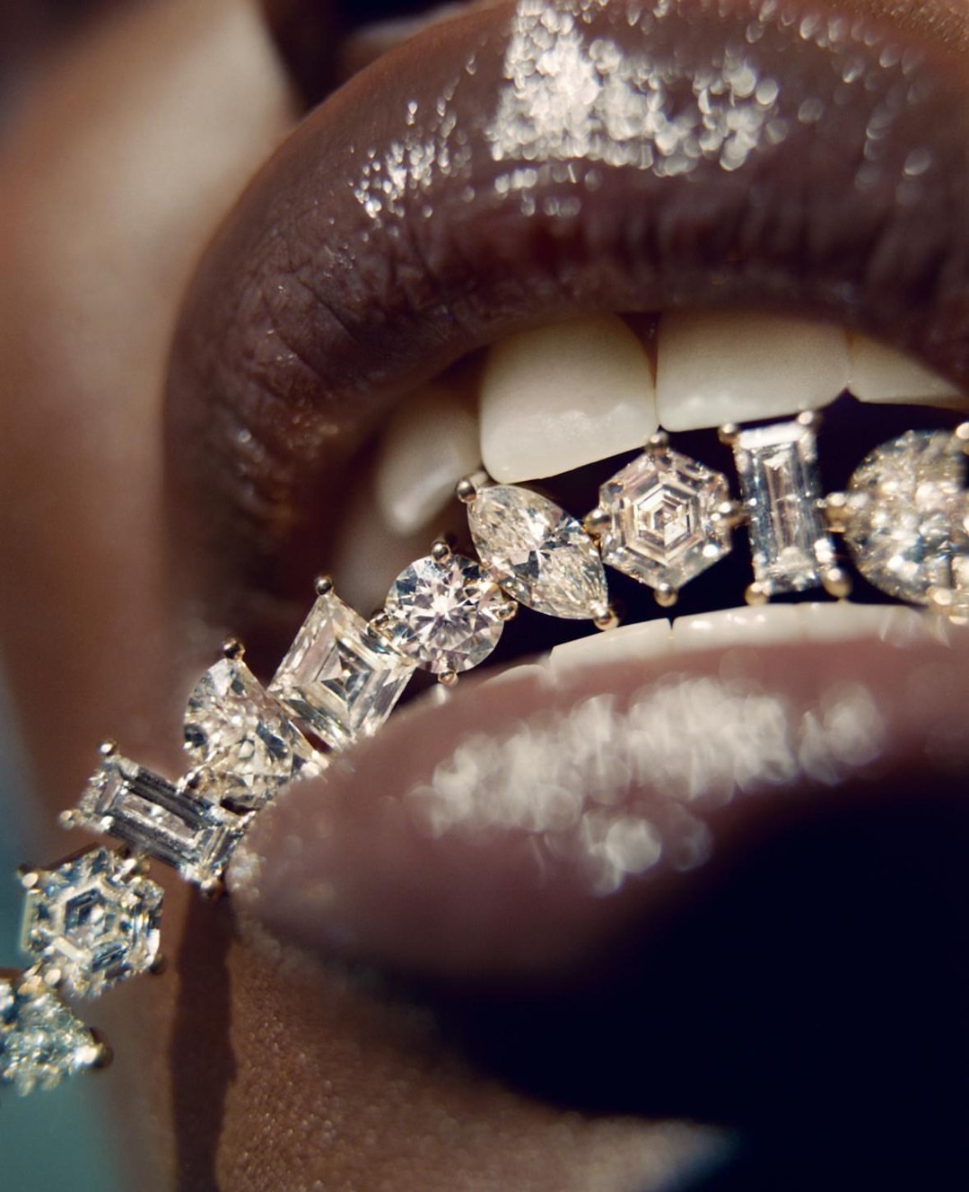 Close-up on dark-skinned woman with glossy lips wearing diamond grill on lower teeth, high-key light, focused on jewelry details.