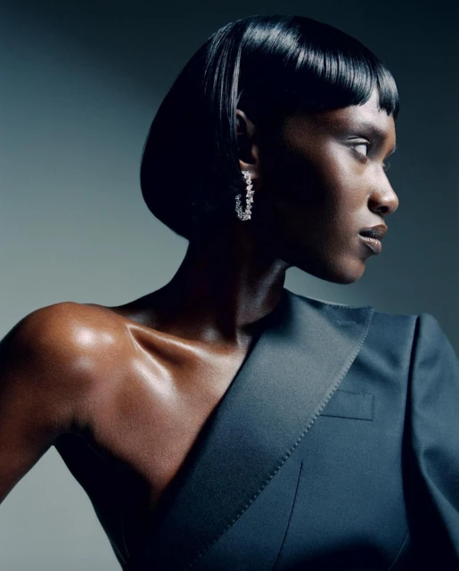 Elegant portrait of an African American female model with short black hair and diamond earrings, wearing a stylish blazer in a studio.