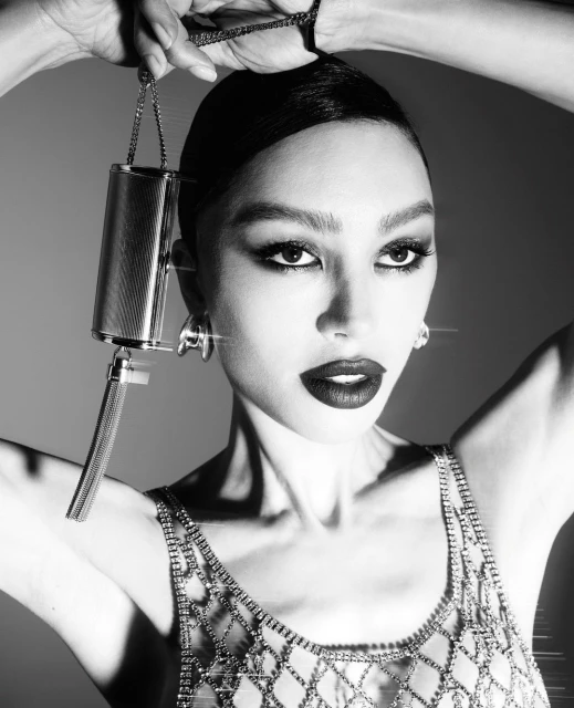 Black and white portrait of a stylish woman holding a silver cylindrical purse with chain details, posing in a photo studio setting.
