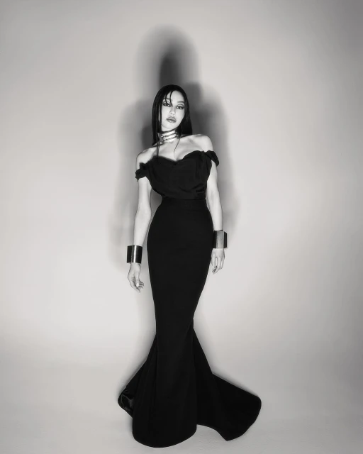 Woman in black off-the-shoulder dress with silver choker and bracelets poses in a photo studio. Black and white fashion shot.