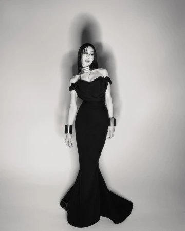 Woman in black off-the-shoulder dress with silver choker and bracelets poses in a photo studio. Black and white fashion shot.