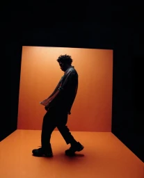 Silhouette of a man walking across a vibrant orange studio set photographed by Sasha Samsonova