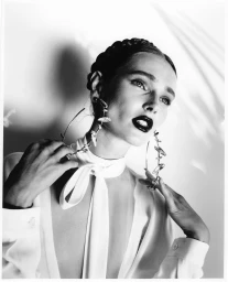 Monochrome portrait of a woman wearing large sculptural hoop earrings and a white blouse with a tie neck.